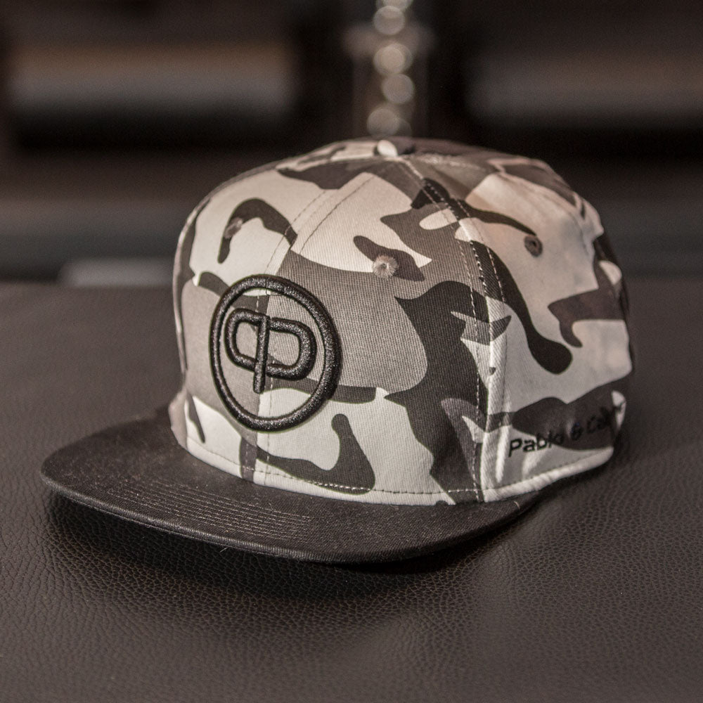 Pablo & Capone white camo snapback cap with embroidered logo on a dark background.