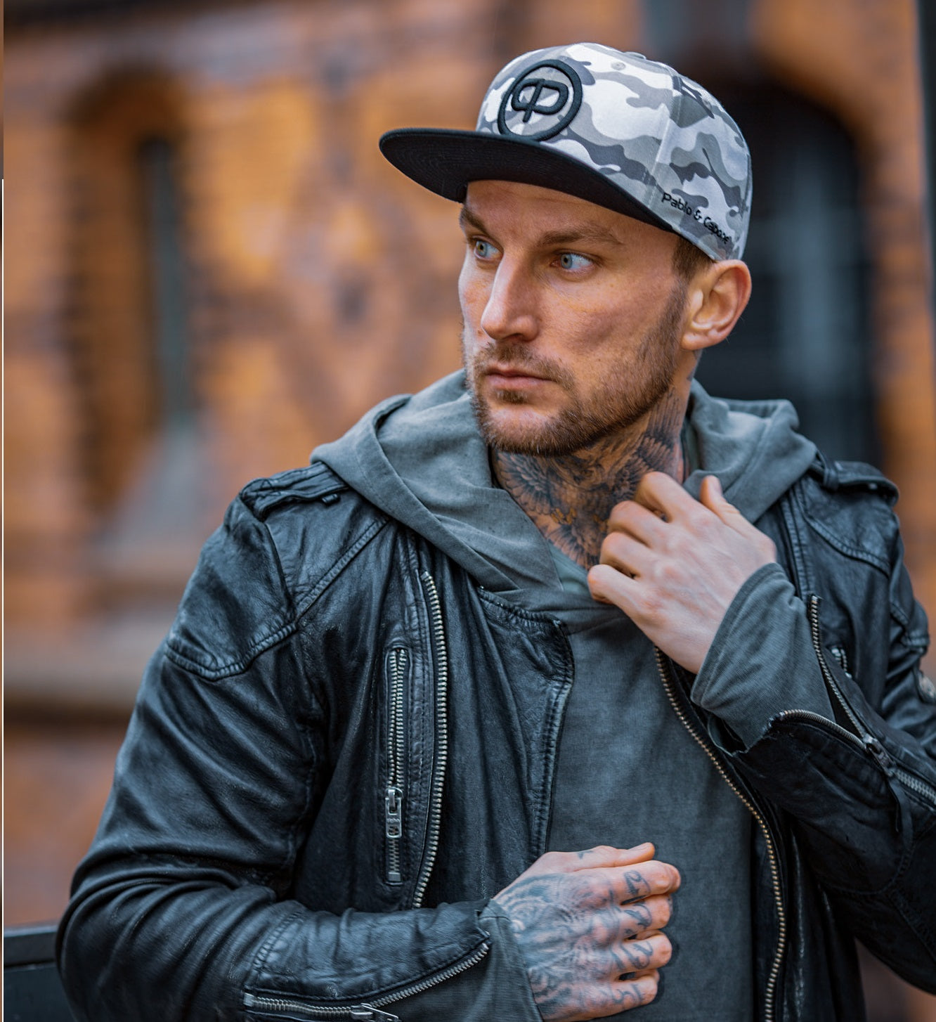 Man wearing a Pablo & Capone white camo snapback cap and leather jacket, showcasing stylish urban fashion.